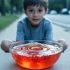 A child holds a clear bowl of jelly that wobbles as if the ground beneath it is vibrating.